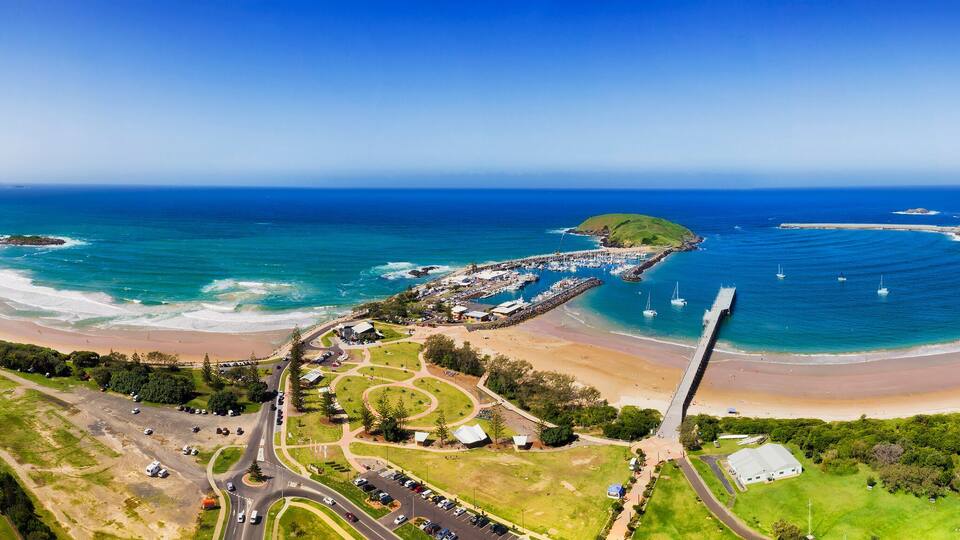 A coastal town with a beach, marina, and surrounding greenery.
