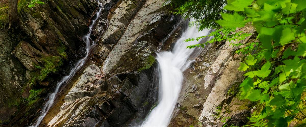 A waterfall cascading over rocky terrain into a calm pool surrounded by lush greenery.