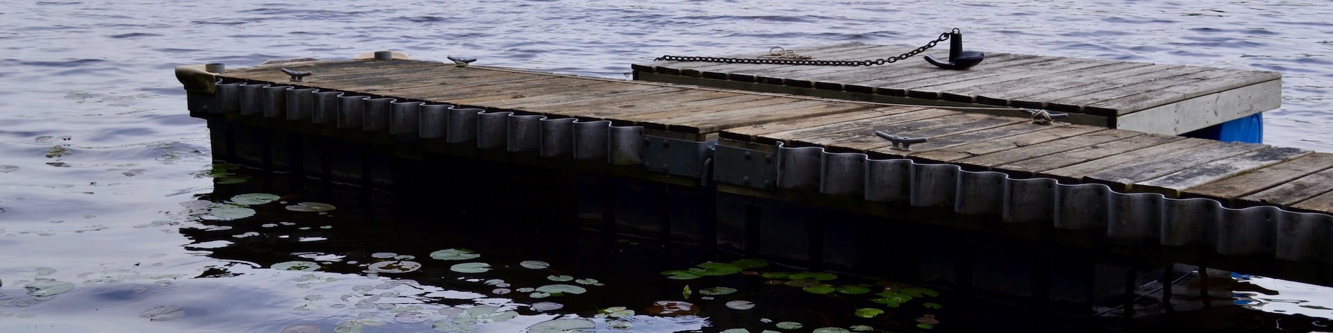 Un muelle de madera que se adentra en un lago con lirios flotando en el agua.