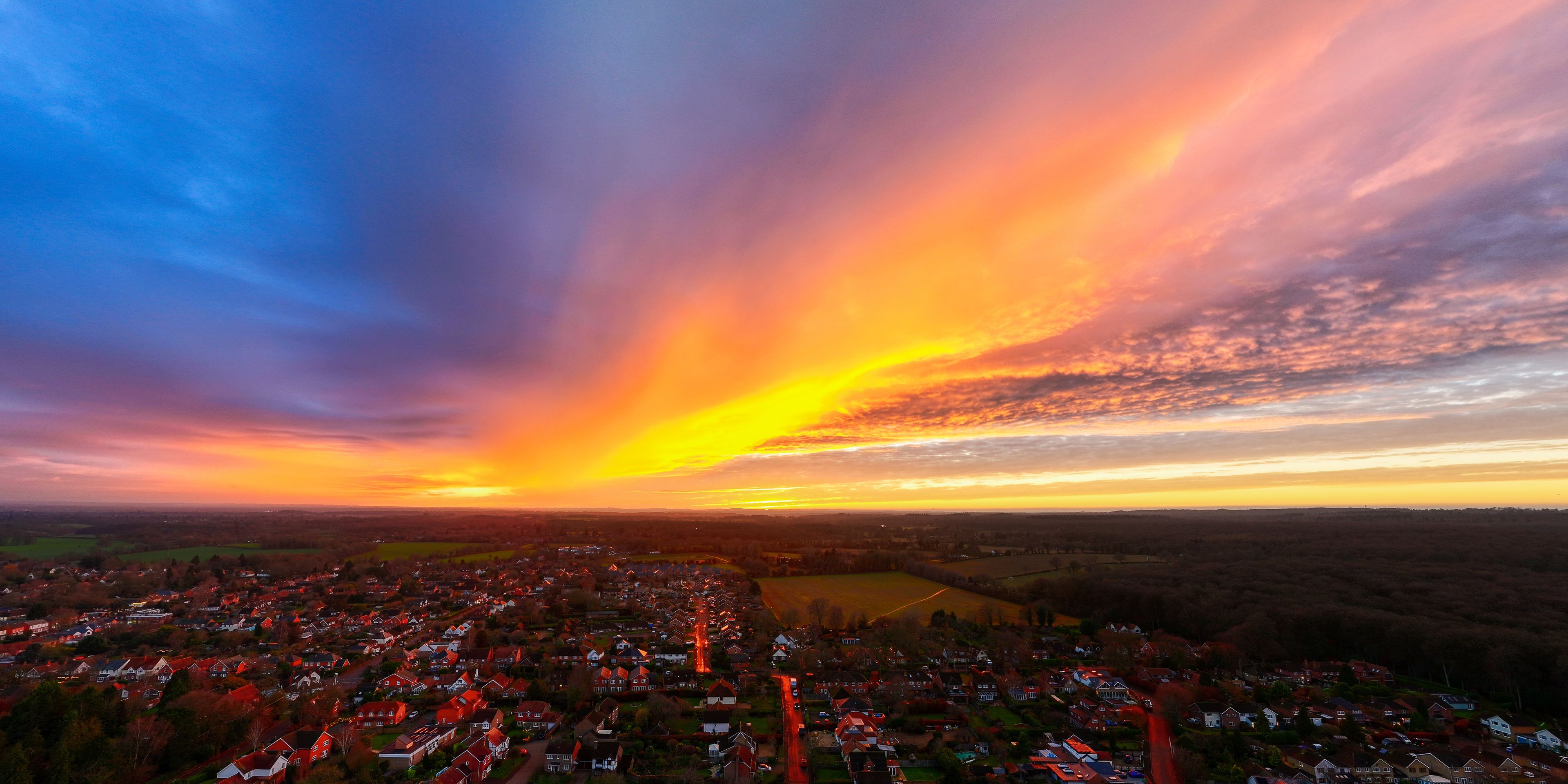Aerial view of a sunset blazing with fiery oranges and yellows over the town, contrasting with the cool blues of the sky, Henley-on-Thames, Oxfordshire, England.