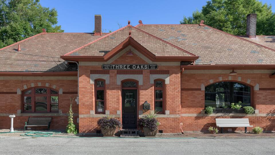 A brick building with a sign reading "Chicago Three Oaks" and "Detroit Miles".