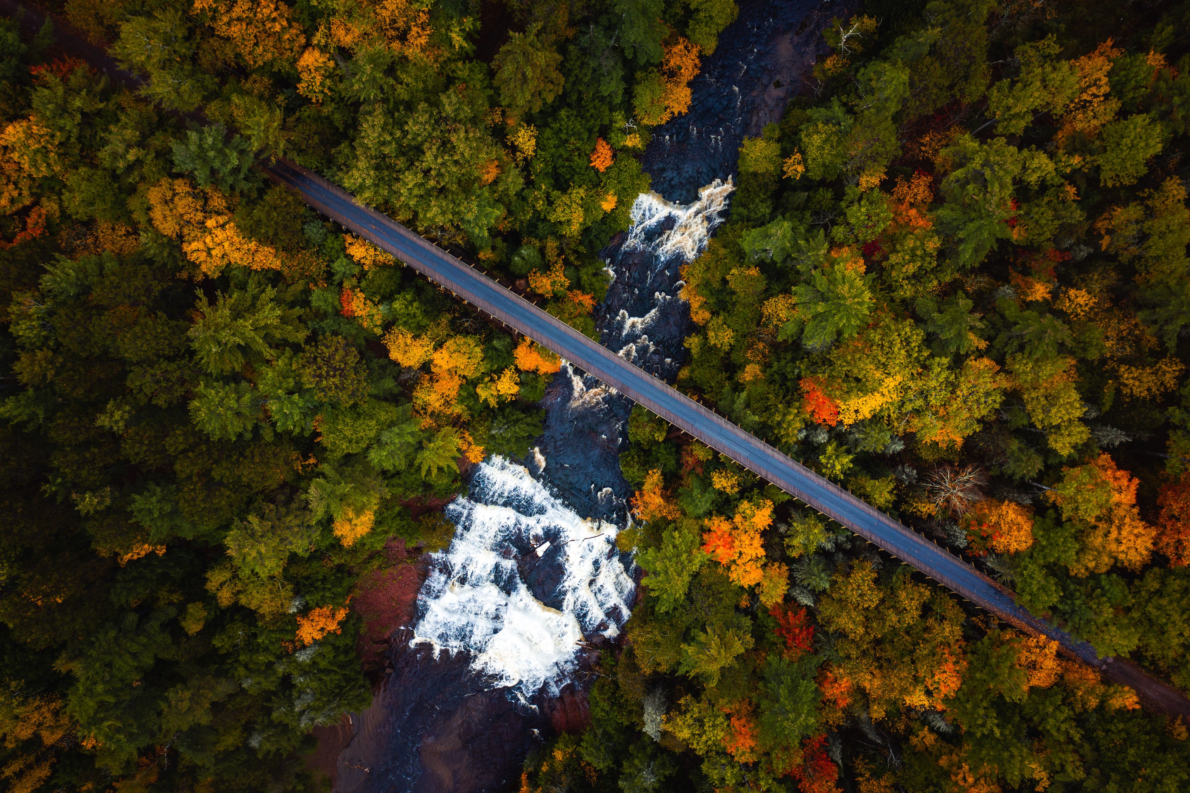 Beautiful look down travel aerial photograph of the abandoned railroad bridge crossing the Ontonagon River and scenic Agate Falls waterfall below surrounded by forest of evergreen and deciduous trees.