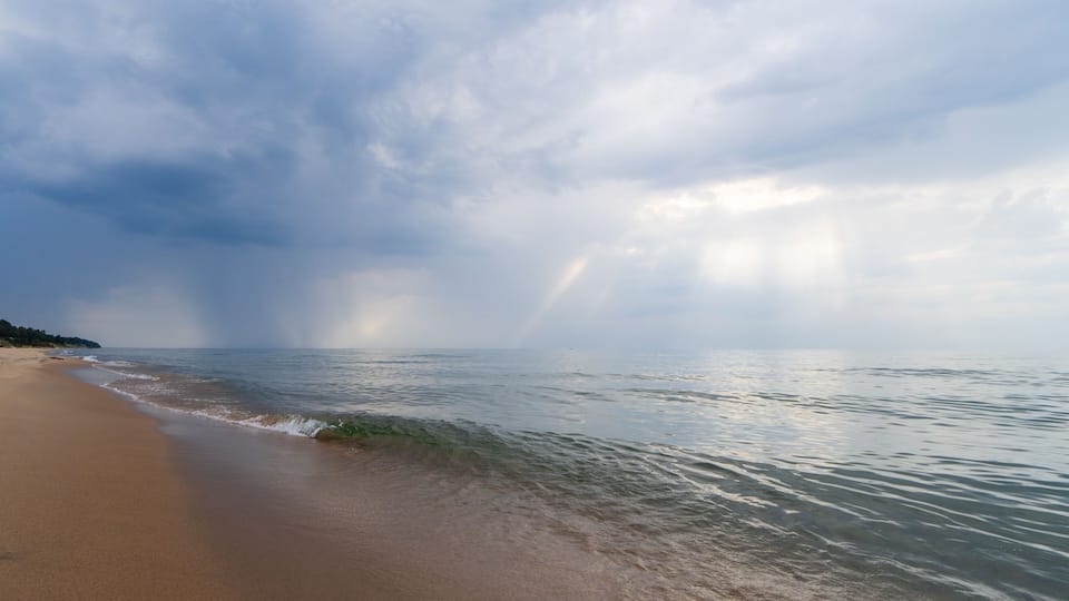A beach with waves, a rainbow, and a cloudy sky.