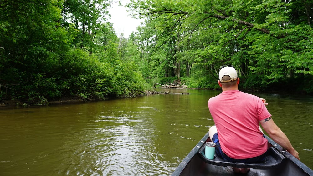 A man in a canoe on a river surrounded by dense green forest.