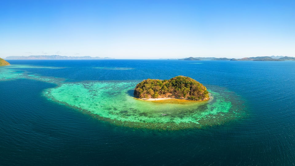 An aerial view of a tropical island surrounded by clear blue waters with a coral reef.