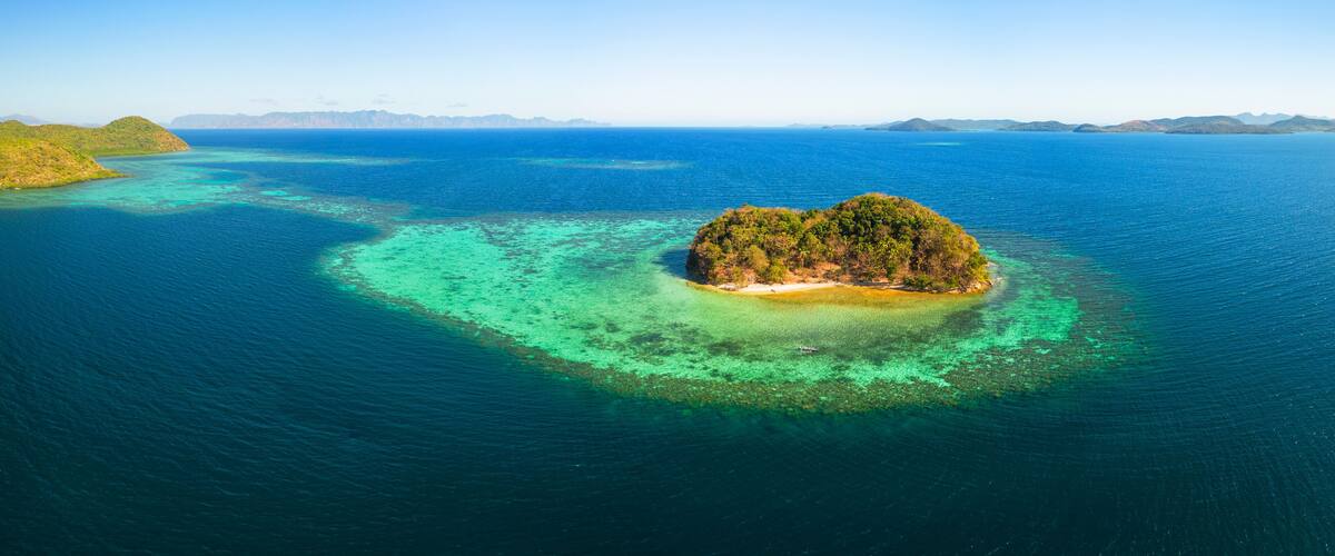 An aerial view of a tropical island surrounded by clear blue waters with a coral reef.