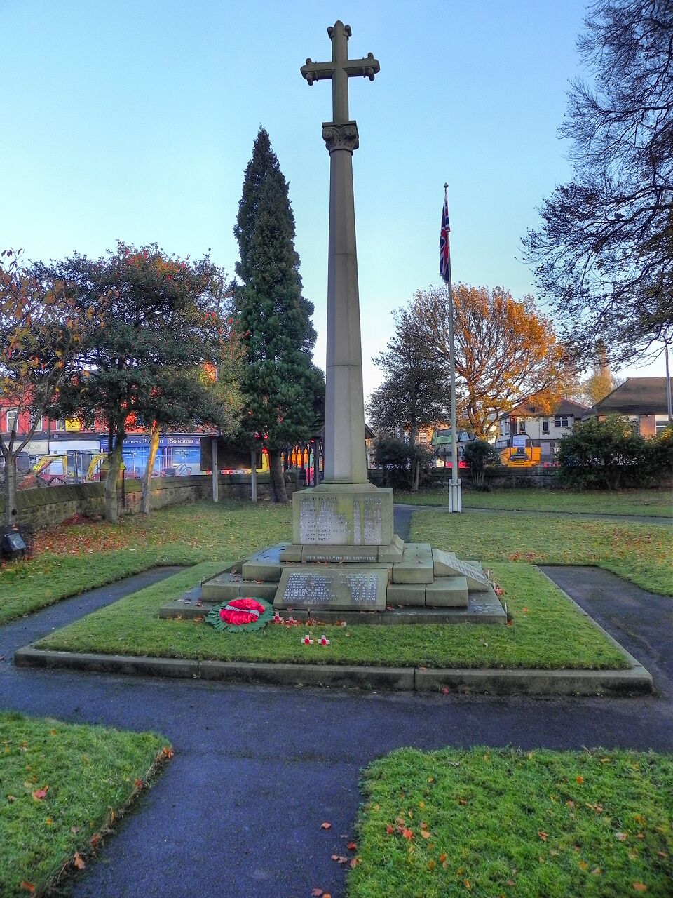 A war memorial with a cross, surrounded by grass and trees.