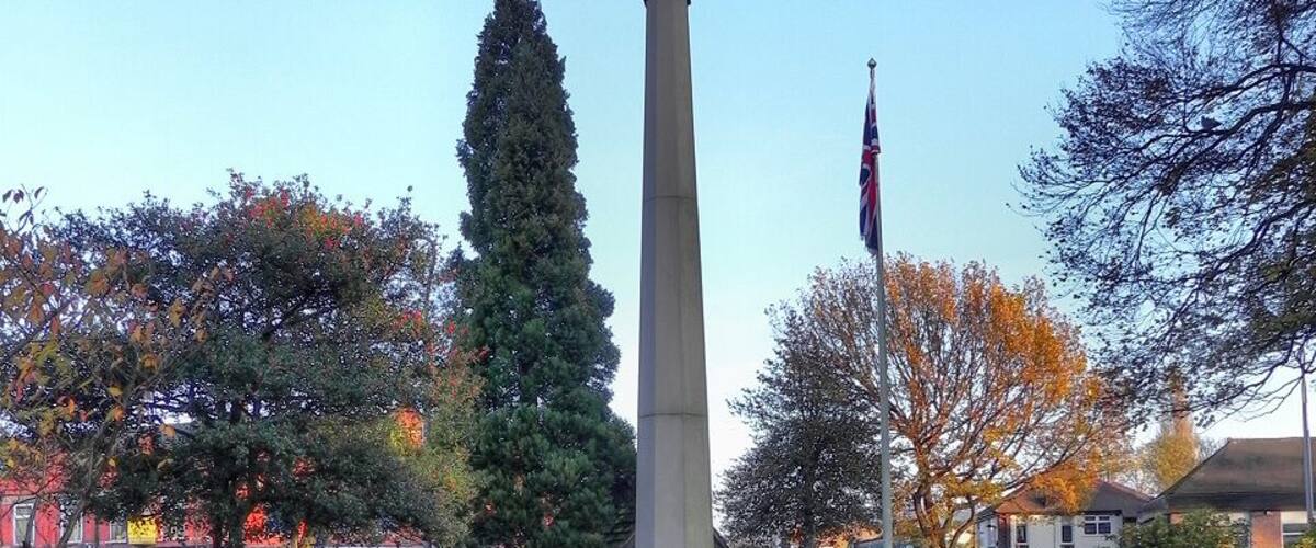 A war memorial with a cross, surrounded by grass and trees.