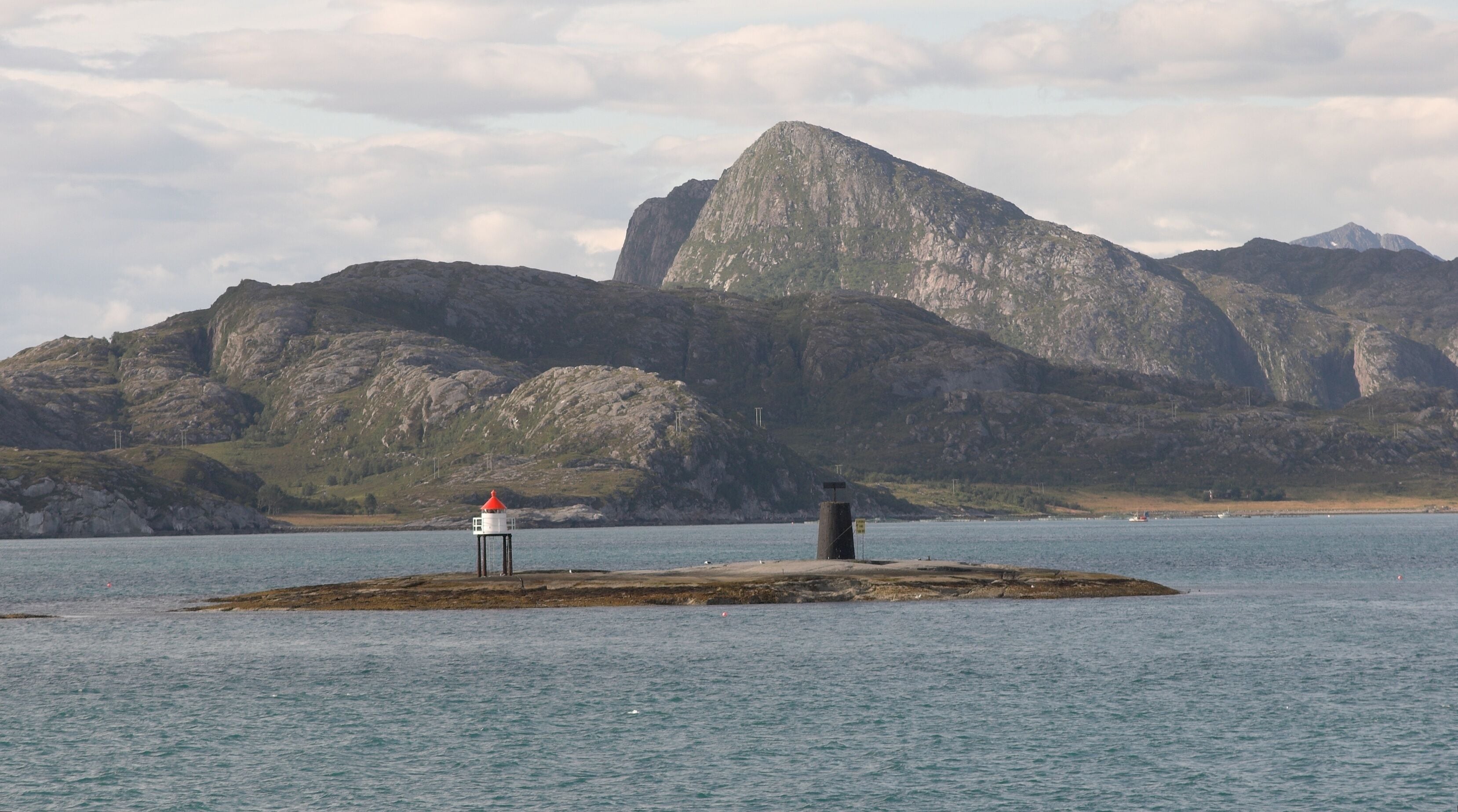 A lighthouse on a rocky island with mountains in the background.
