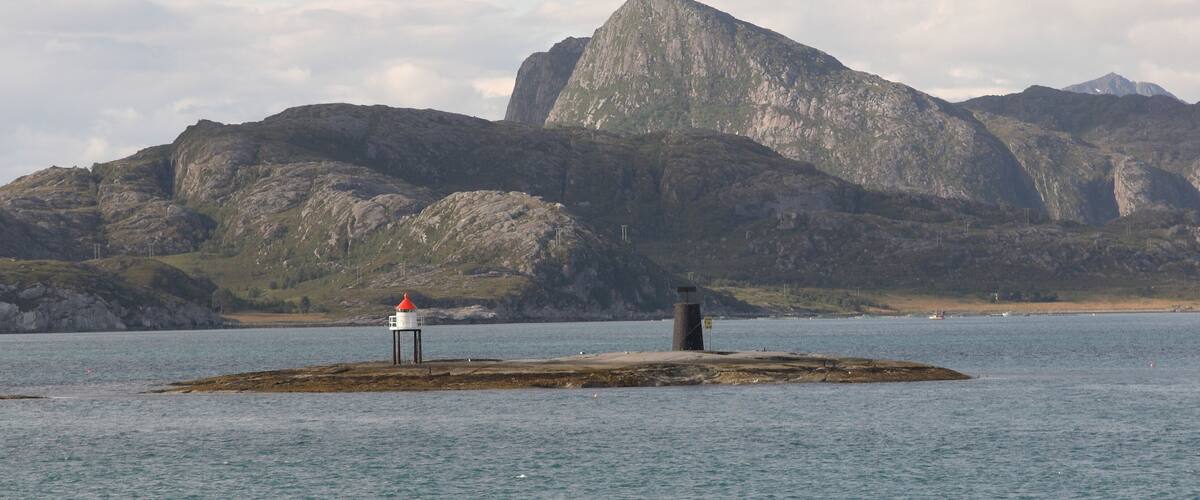 A lighthouse on a rocky island with mountains in the background.