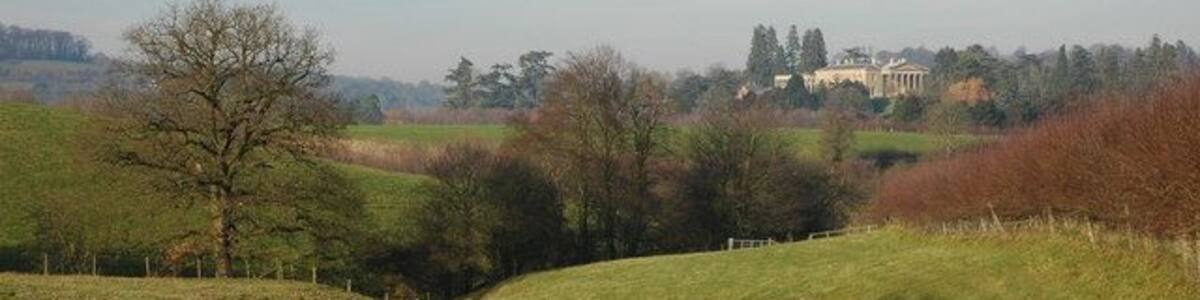 Ein grünes Feld mit einem Hügel, Bäumen und einem entfernten Gebäude.