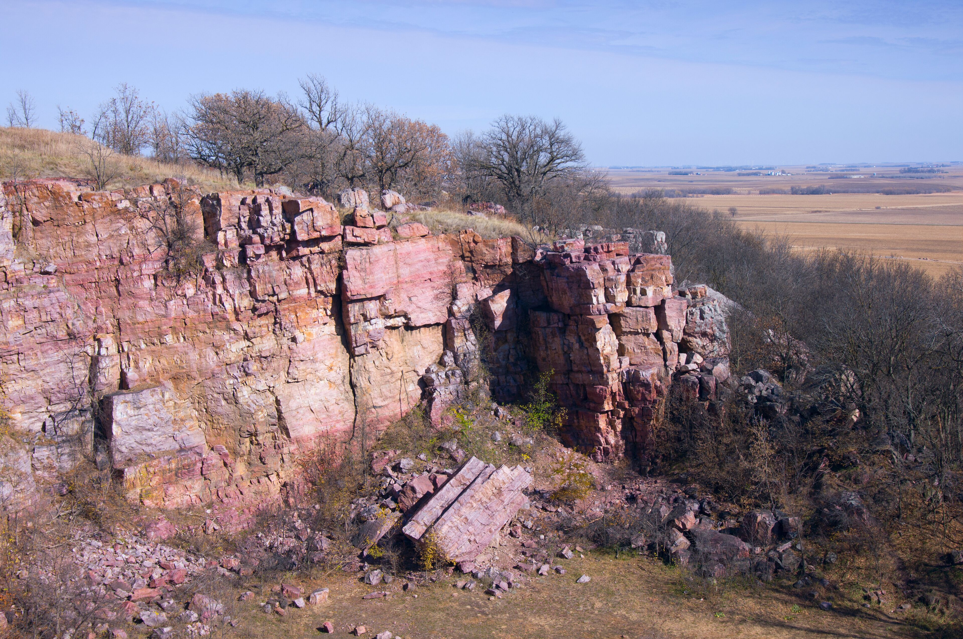 A rocky cliff with sparse vegetation and a distant view of a flat landscape.