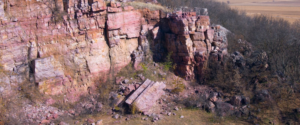 A rocky cliff with sparse vegetation and a distant view of a flat landscape.