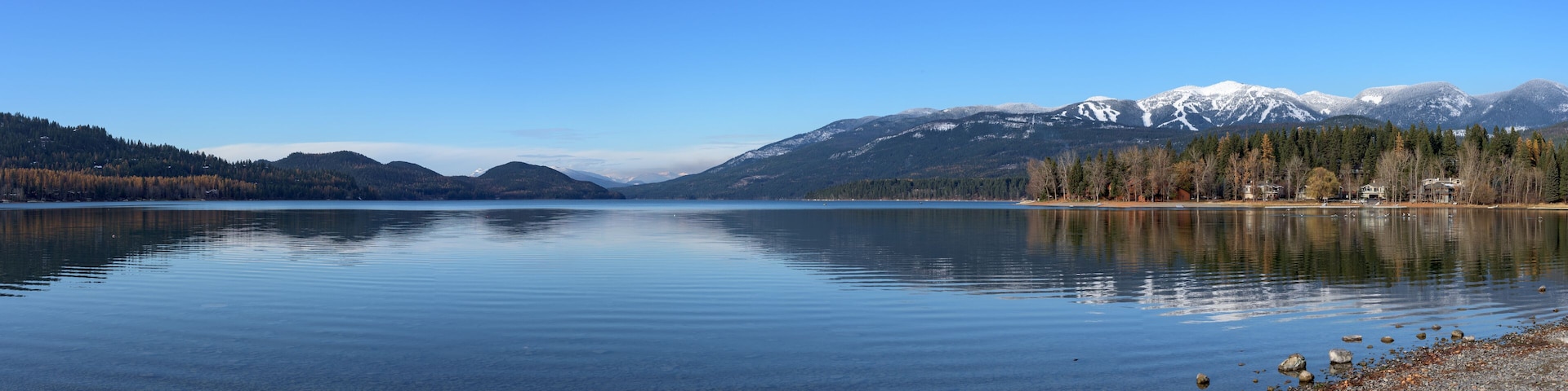 A calm lake with a rocky shoreline, surrounded by mountains and trees.