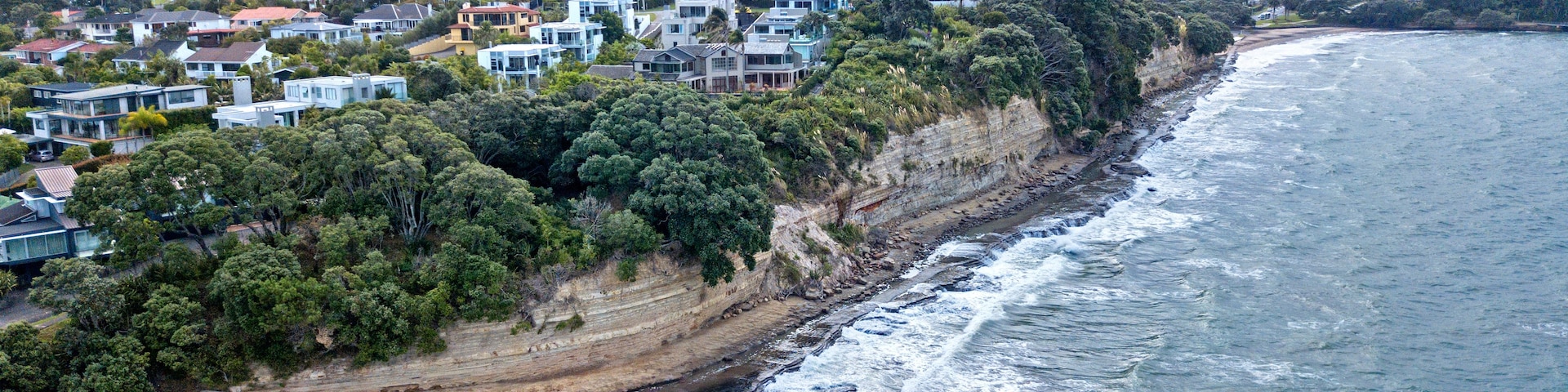 Uma área residencial costeira com casas ao longo do penhasco, uma praia e o oceano.