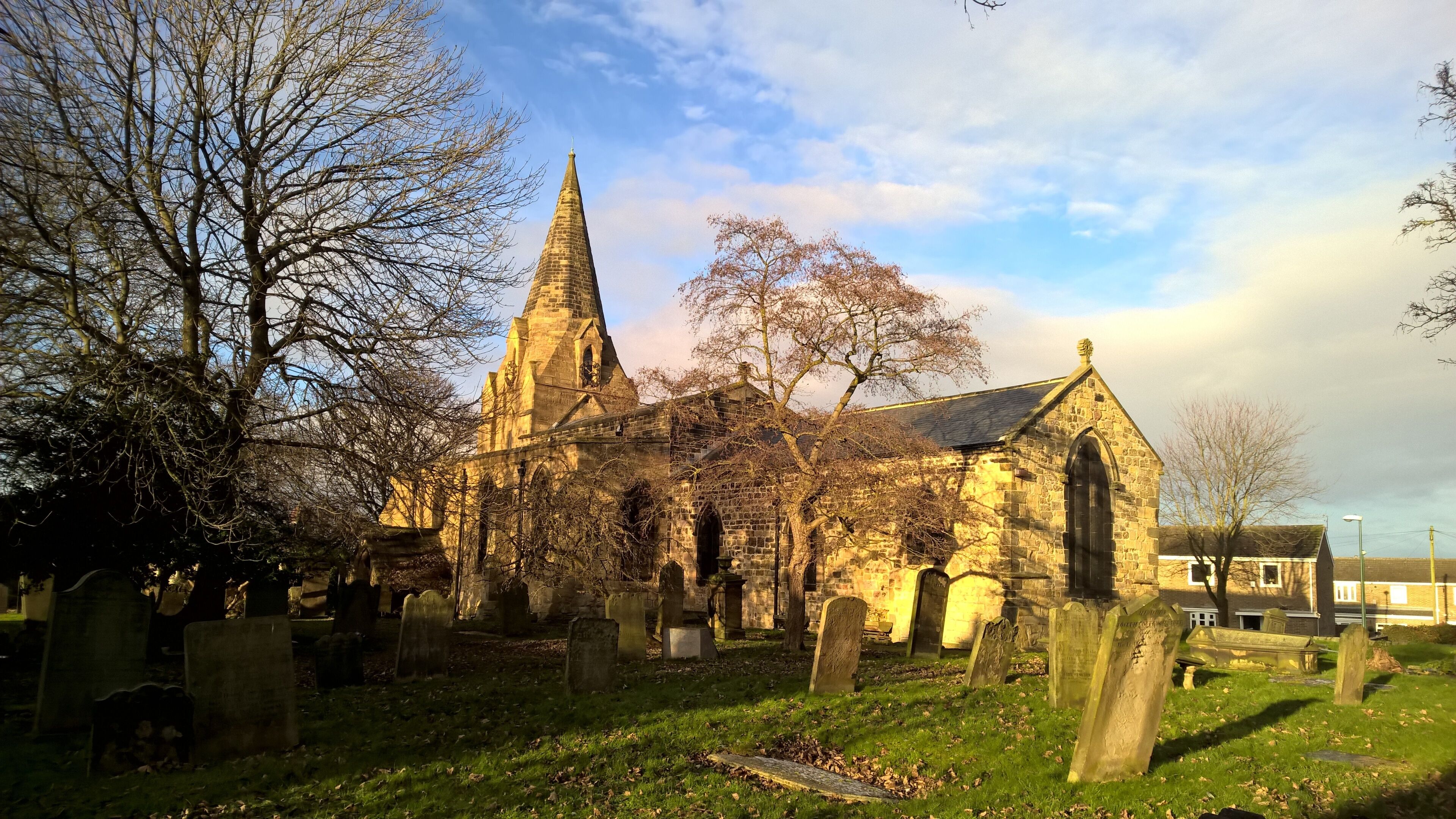 A historic church with a tall spire and stone walls, surrounded by a cemetery with headstones.