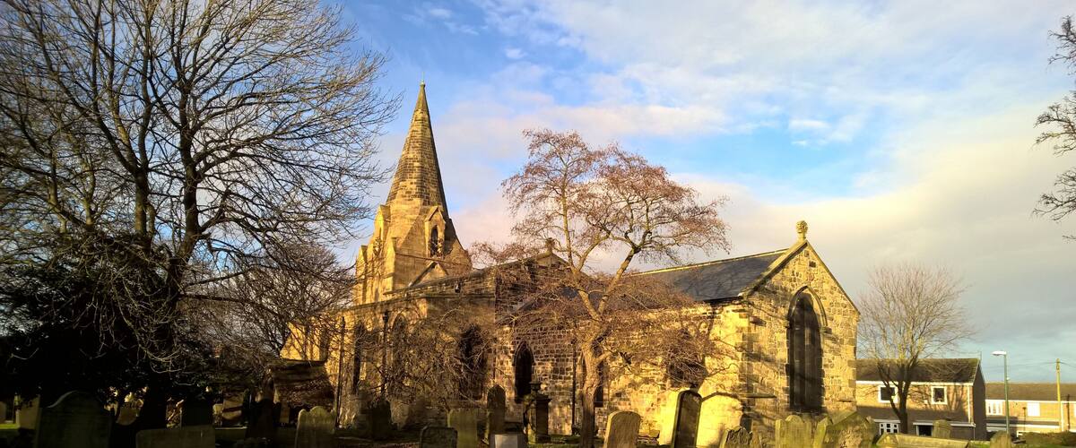 A historic church with a tall spire and stone walls, surrounded by a cemetery with headstones.