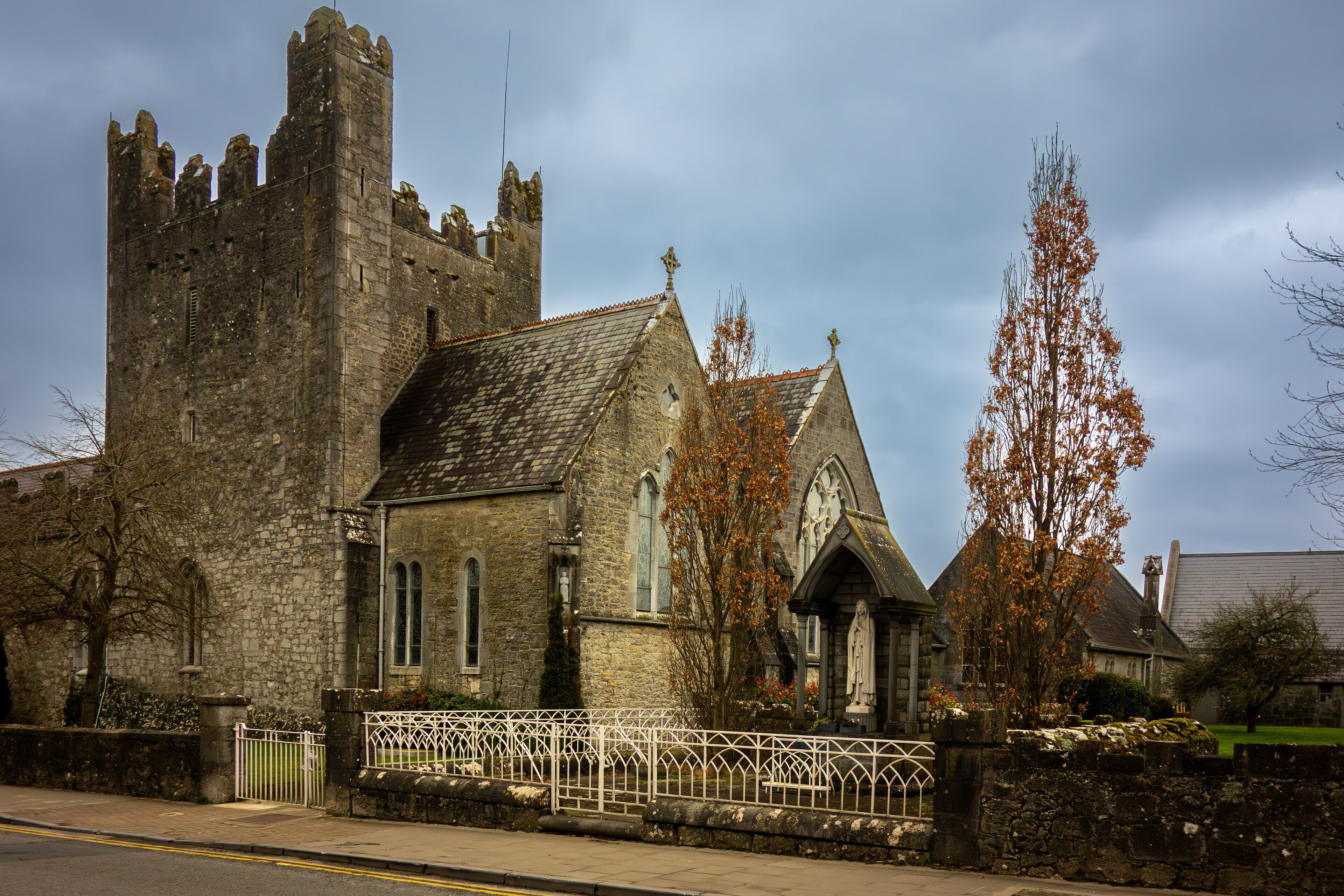 A historic stone church with a tall bell tower and a white fence in front.