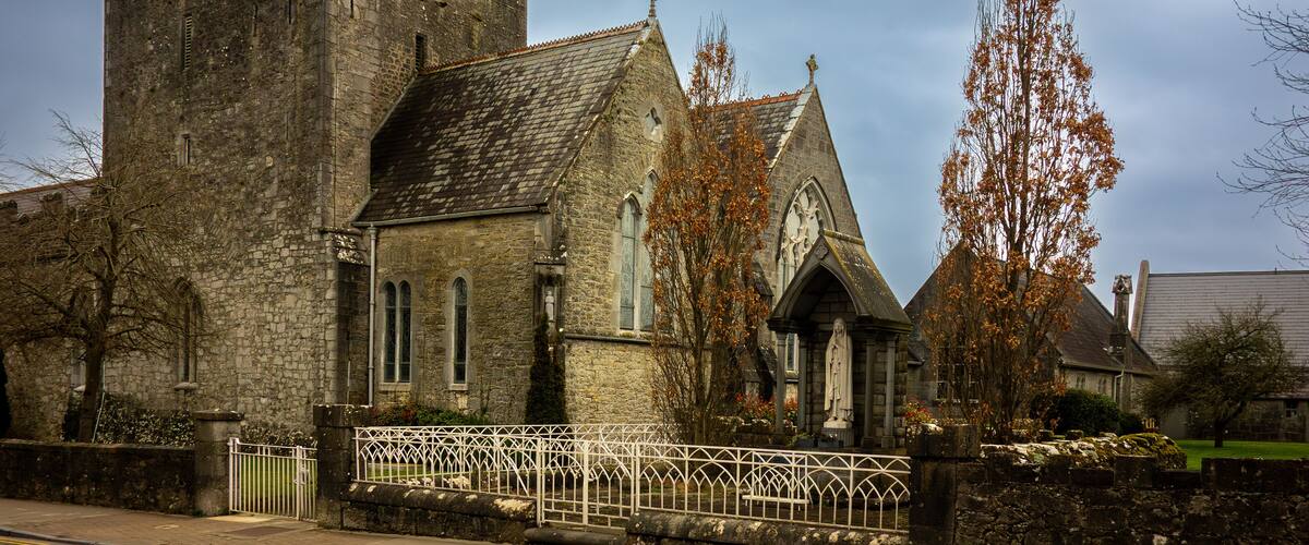 A historic stone church with a tall bell tower and a white fence in front.