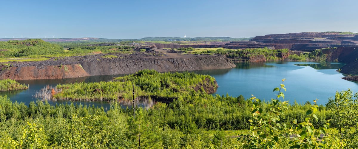 A landscape with a large body of water surrounded by green vegetation and mining areas.
