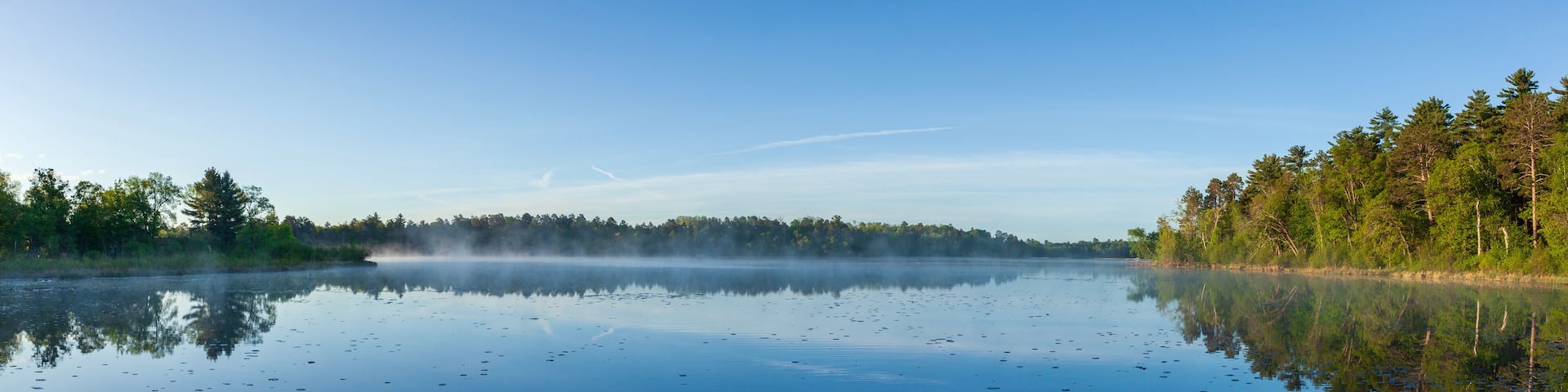 Panorama of a calm lake at dawn with pines on the shore in northern Minnesota