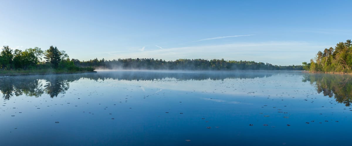 A calm lake with reflections of trees and a clear sky.