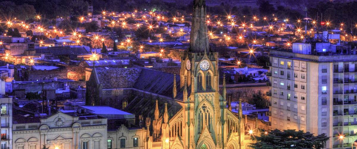 A cathedral with a tall spire, surrounded by a cityscape with illuminated streets and buildings.