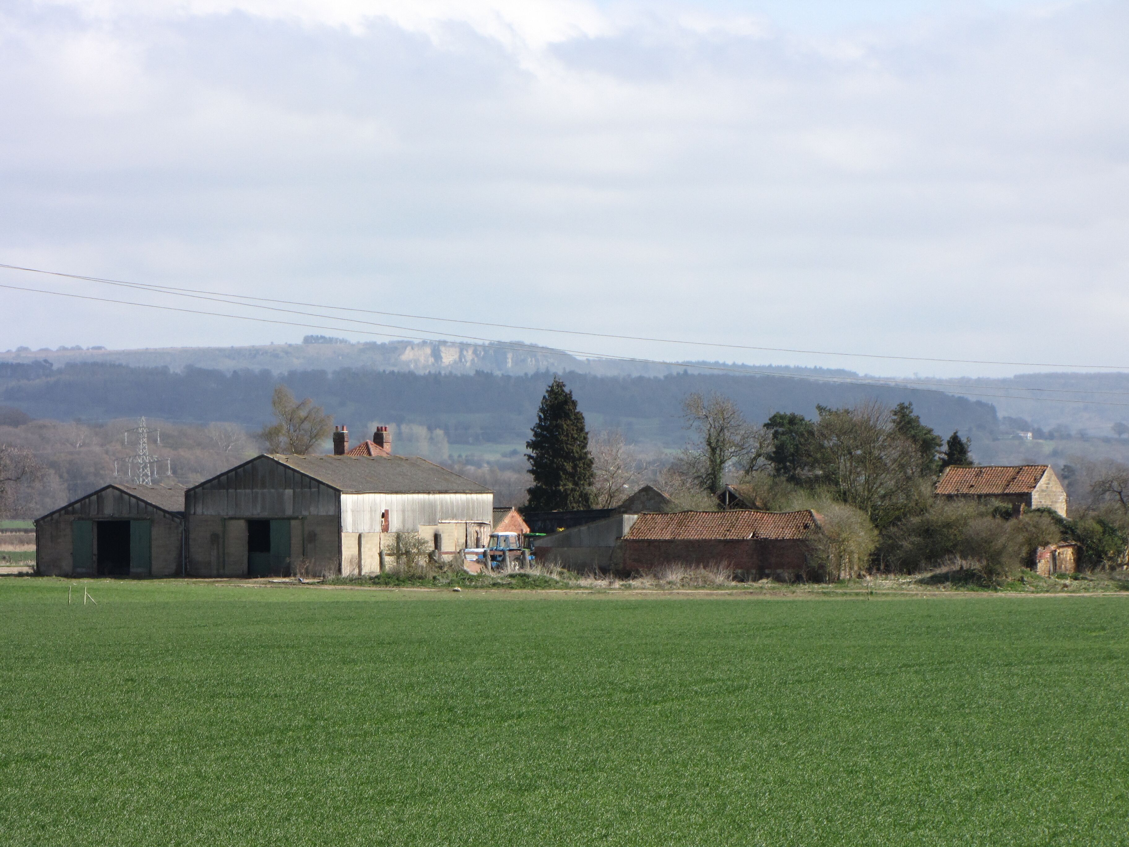 A rural landscape with green fields, several farm buildings, and distant hills.