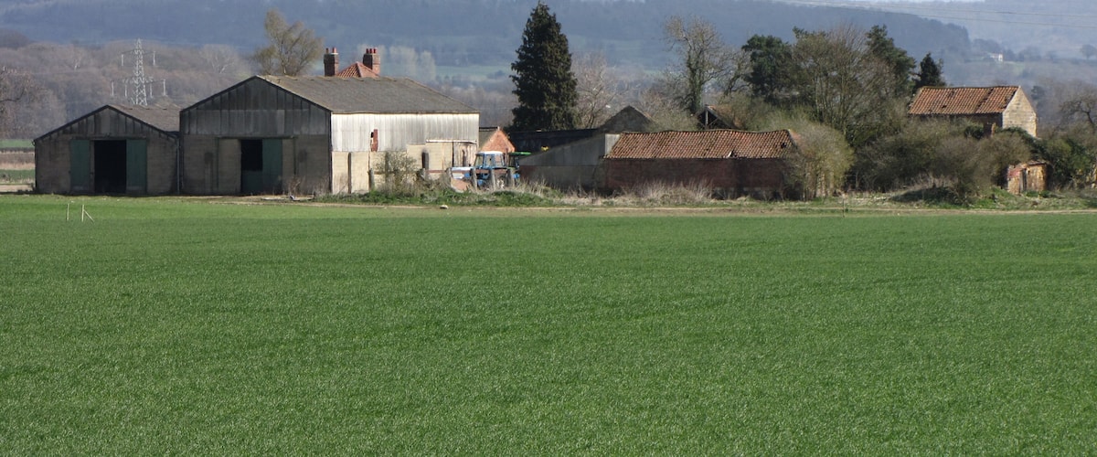 A rural landscape with green fields, several farm buildings, and distant hills.