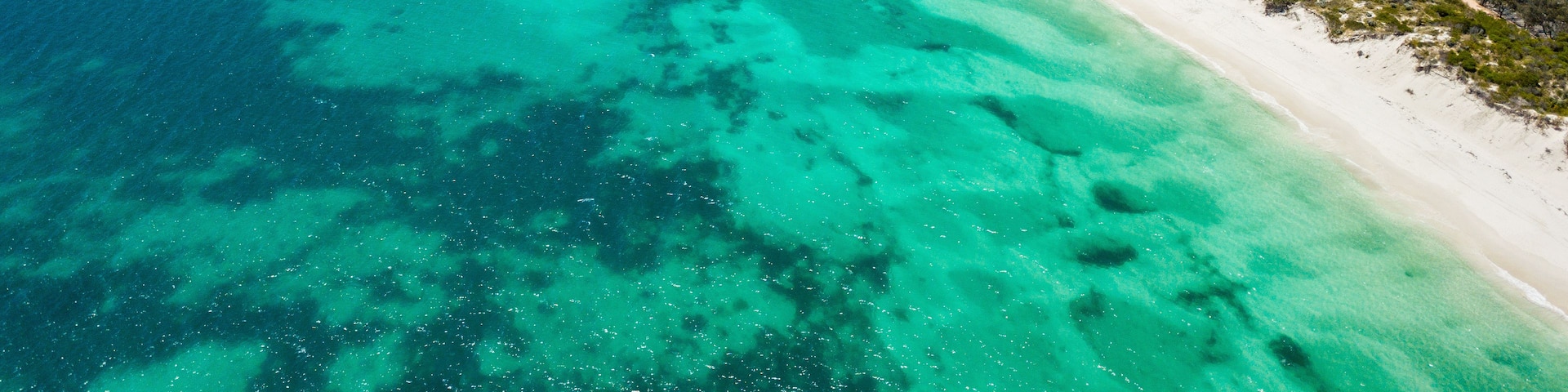 A coastal town with a beach, clear turquoise waters, and a dense residential area.