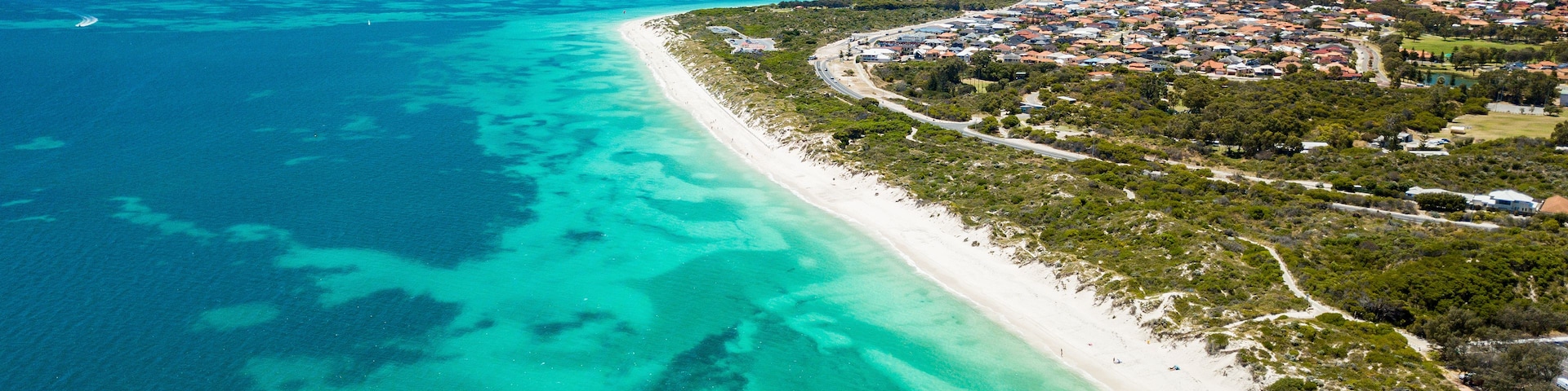 Eine Küstenstadt mit Strand, klarem türkisblauem Wasser und einem dicht bebauten Wohngebiet.