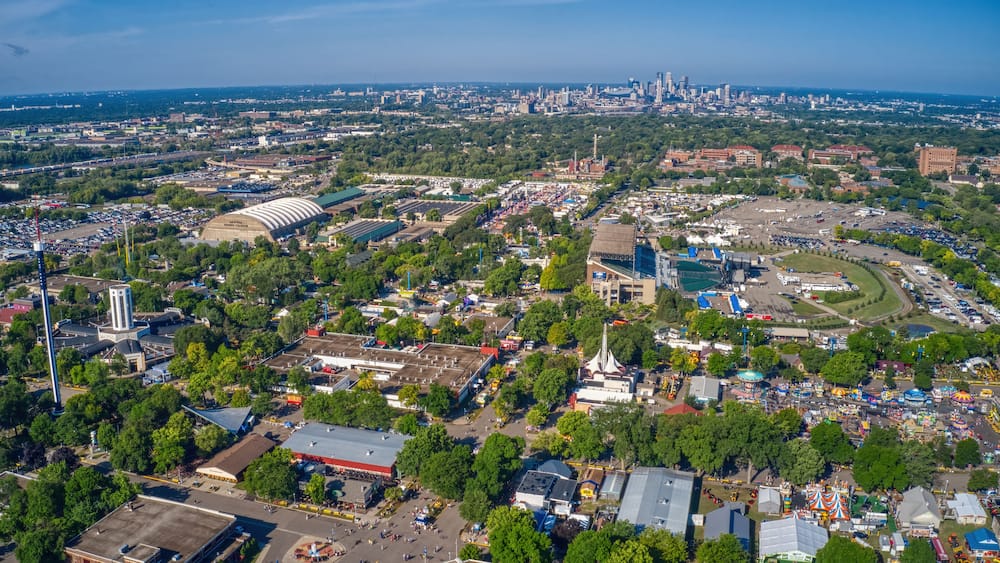 An aerial view of a city with a large stadium, various buildings, and a distant skyline.