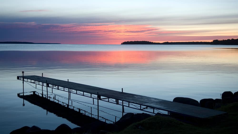 Ein ruhiger See bei Sonnenuntergang, mit einem hölzernen Steg, der sich ins Wasser erstreckt.