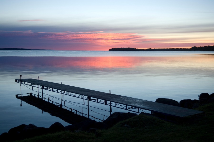 A calm lake at sunset with a wooden dock extending into the water.