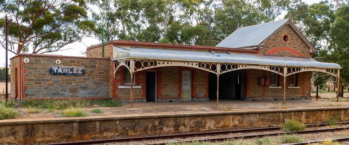 A historic railway station with a stone wall, a covered waiting area, and multiple railway tracks.