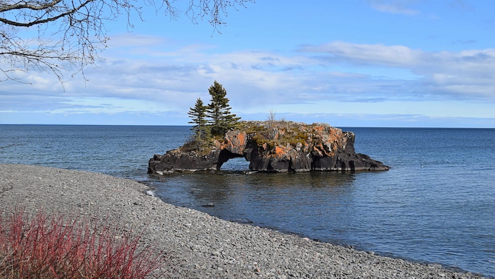 A rocky outcrop with a tree in the center, surrounded by calm water.