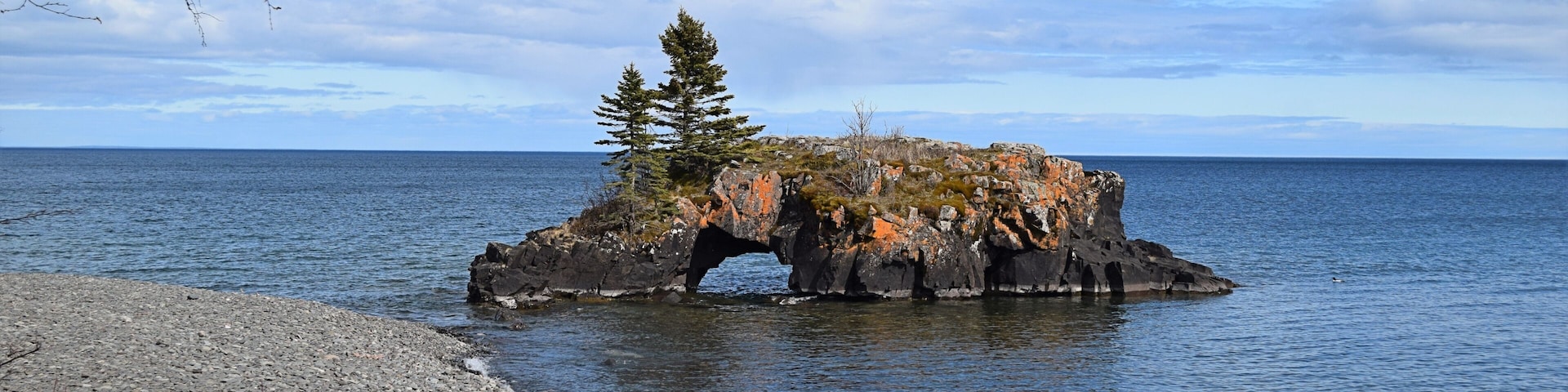 A rocky outcrop with a tree in the center, surrounded by calm water.