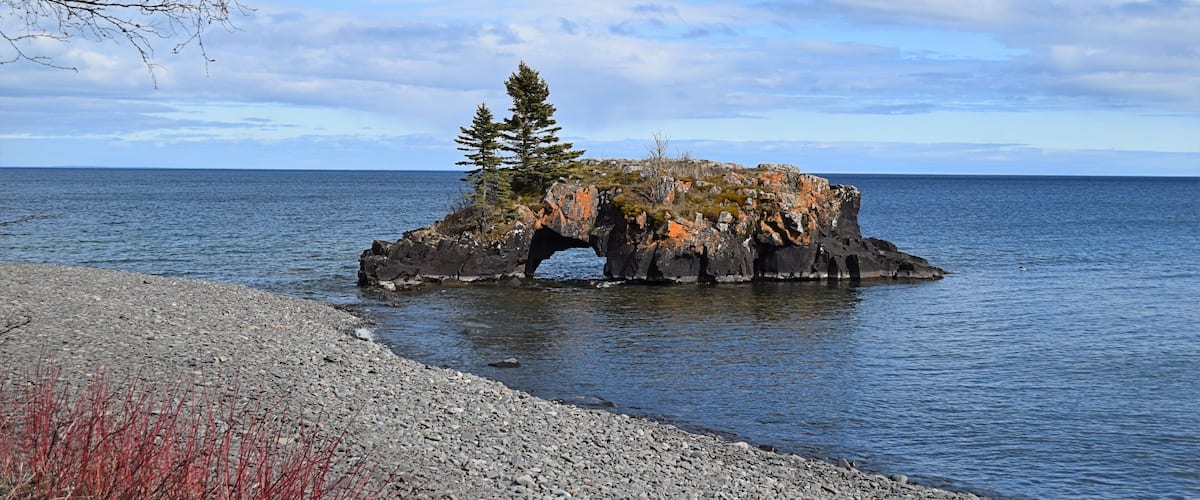 A rocky outcrop with a tree in the center, surrounded by calm water.