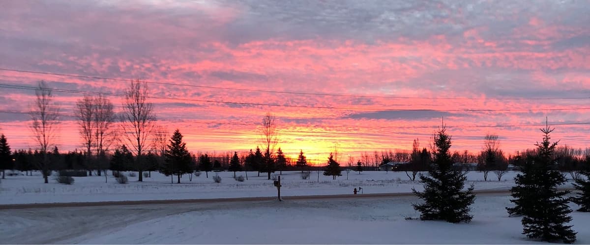 A snowy landscape with a sunset and a road in the foreground.
