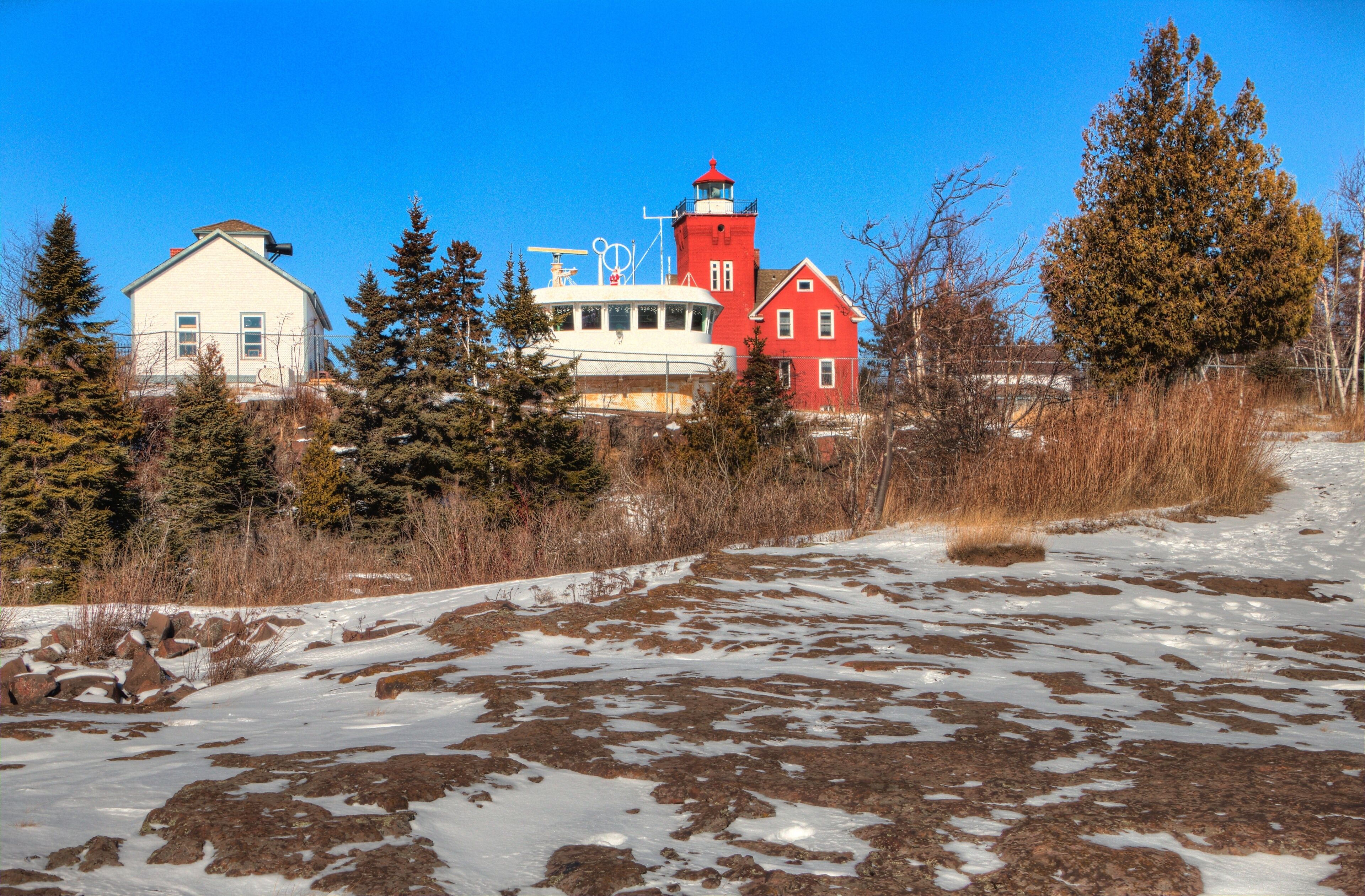 A red lighthouse, a white building, and a yellow building with a snowy landscape and trees.