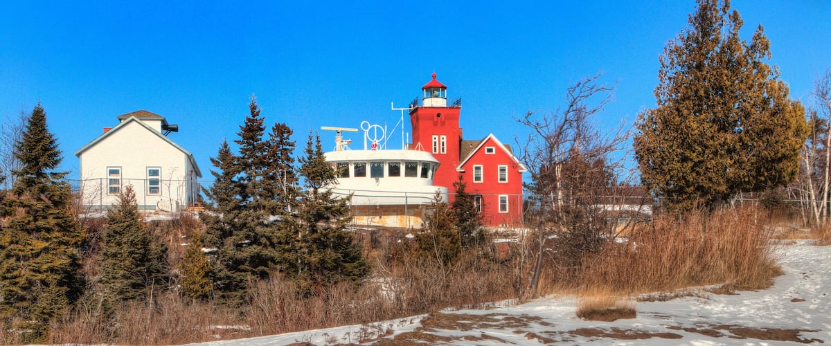 A red lighthouse, a white building, and a yellow building with a snowy landscape and trees.