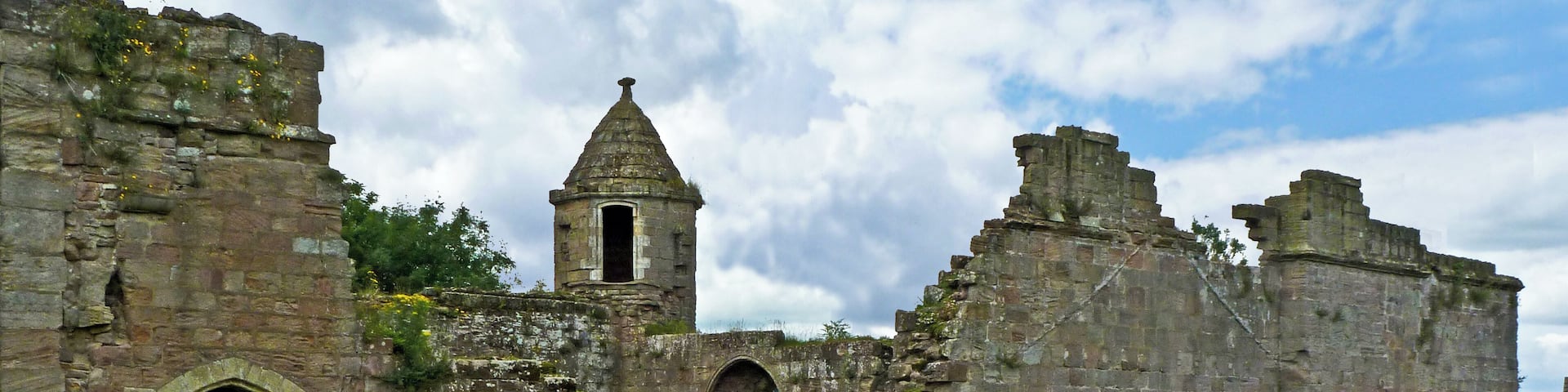 An ancient stone castle with a tower, arched windows, and a grassy field in the foreground.
