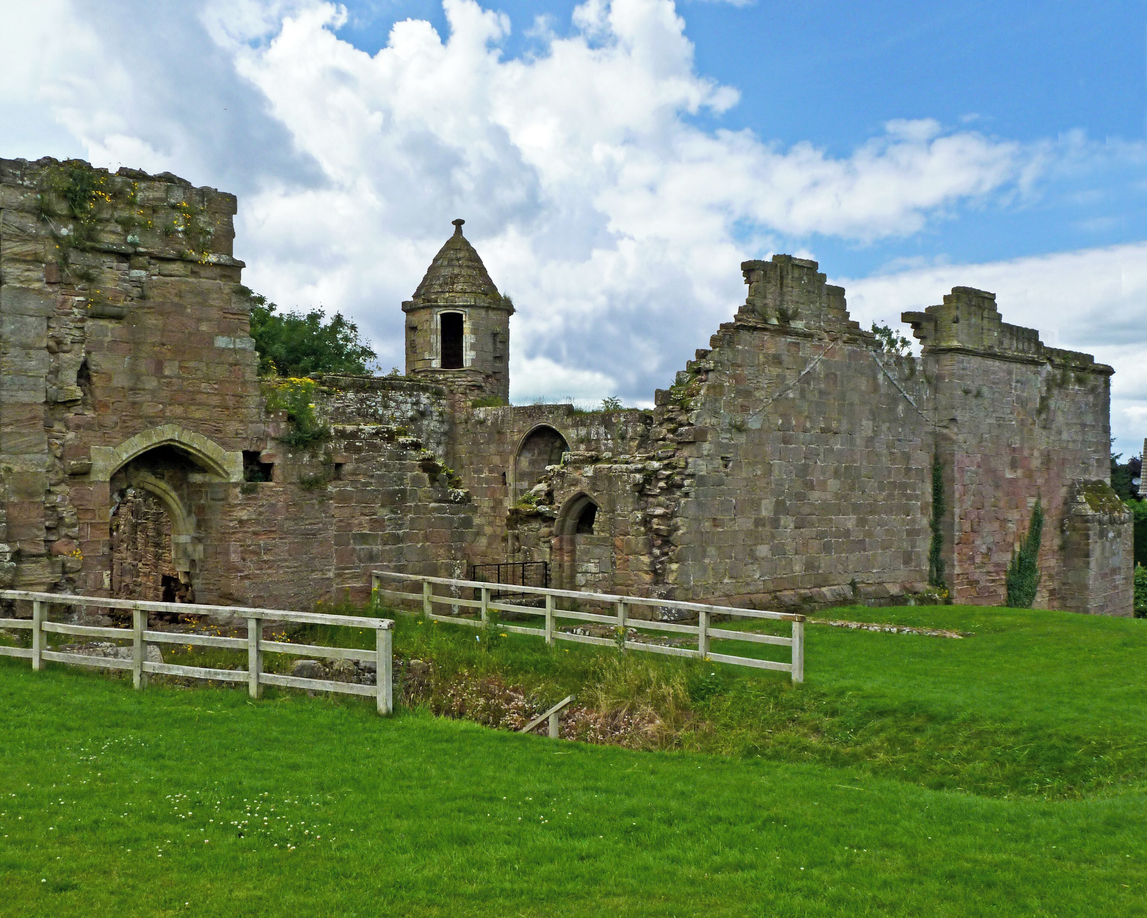 An ancient stone castle with a tower, arched windows, and a grassy field in the foreground.