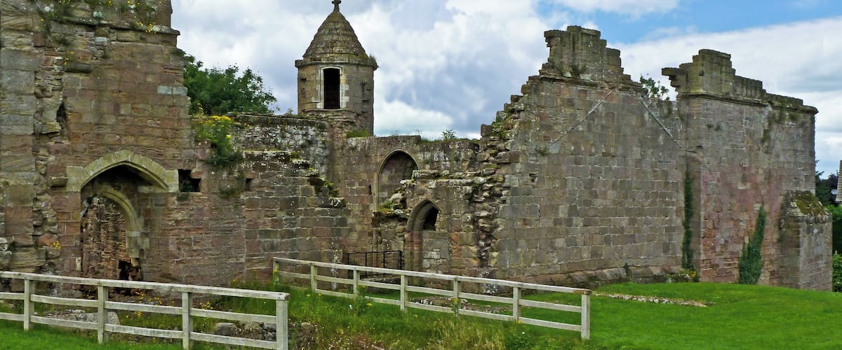 An ancient stone castle with a tower, arched windows, and a grassy field in the foreground.