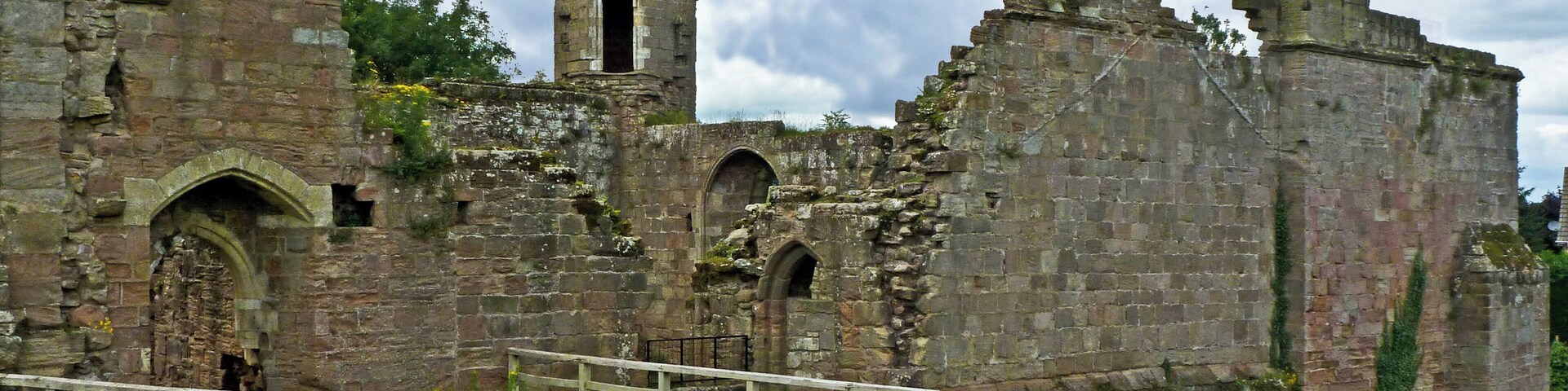 An ancient stone castle with a tower, arched windows, and a grassy field in the foreground.