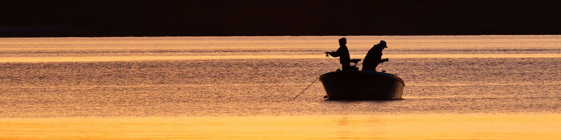 A sunset over a calm body of water with silhouettes of two people on a boat.