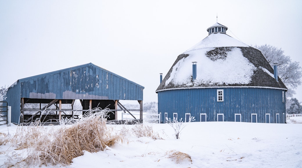 A snow-covered barn and silo in a rural setting.