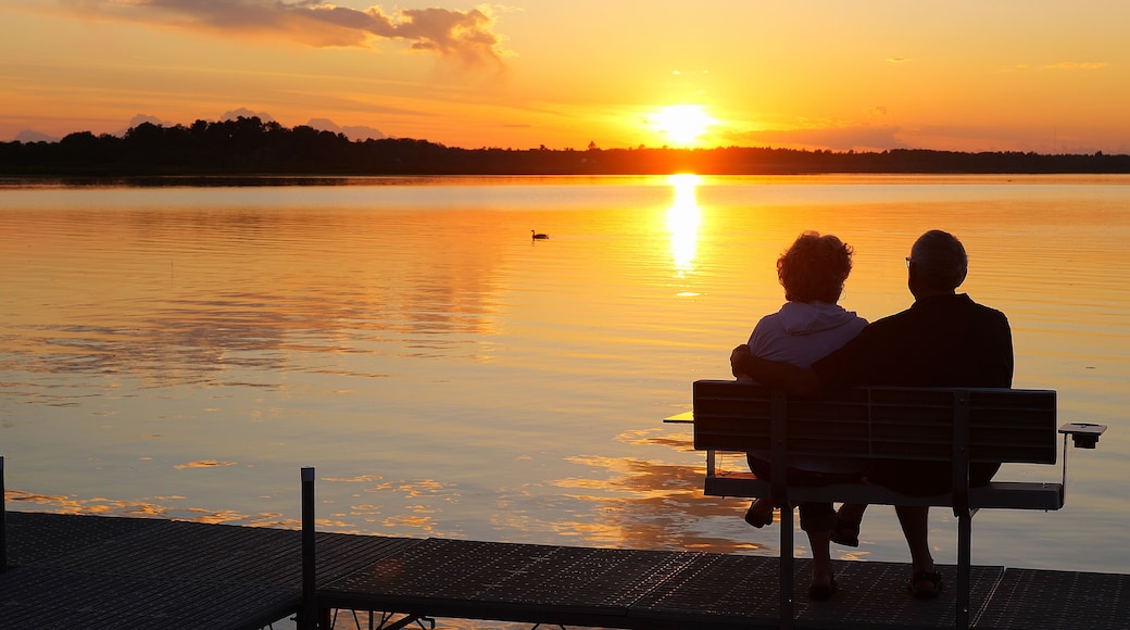 Silhouette of two people on a bench on a dock as they enjoy a sunset over a beautiful lake in Minnesota on a serene and relaxing evening, while a Canada goose swims by on the water.