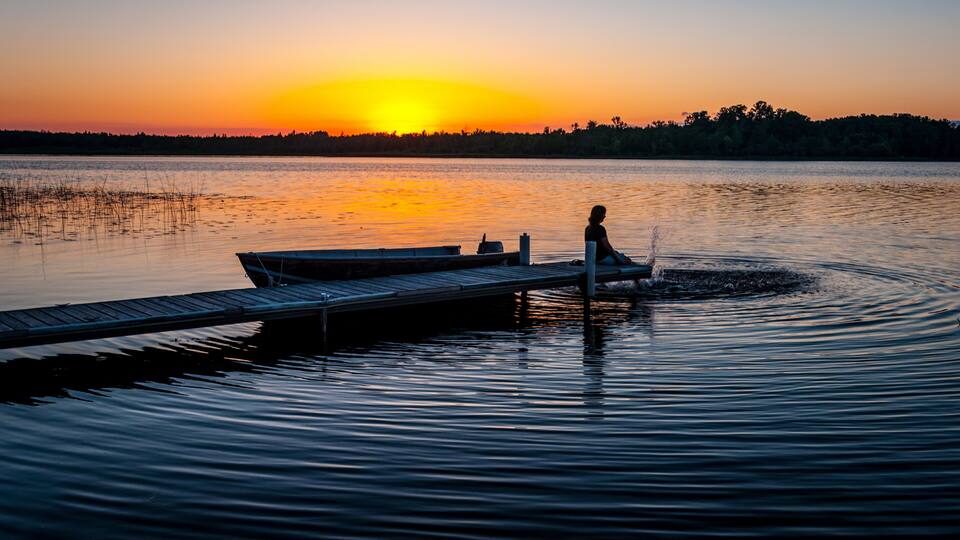 Tranquil silhouette of woman sitting on the dock on the shore of a calm lake in Minnesota