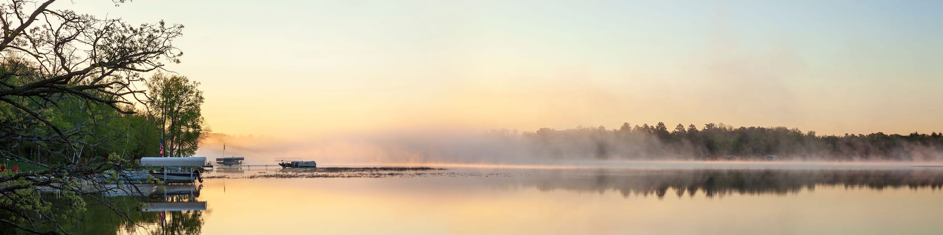 Panorama of a calm northern Minnesota lake and fog at dawn during spring with docks along the shoreline